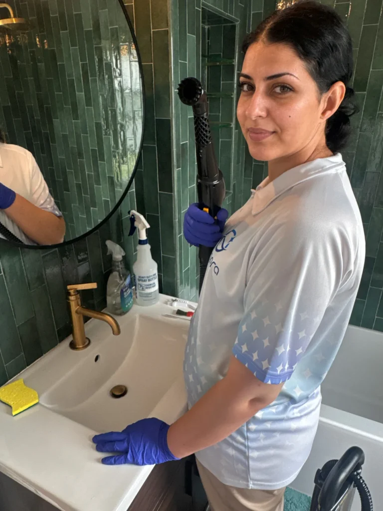 Sygora cleaner at a bathroom sink with a vacuum wand.