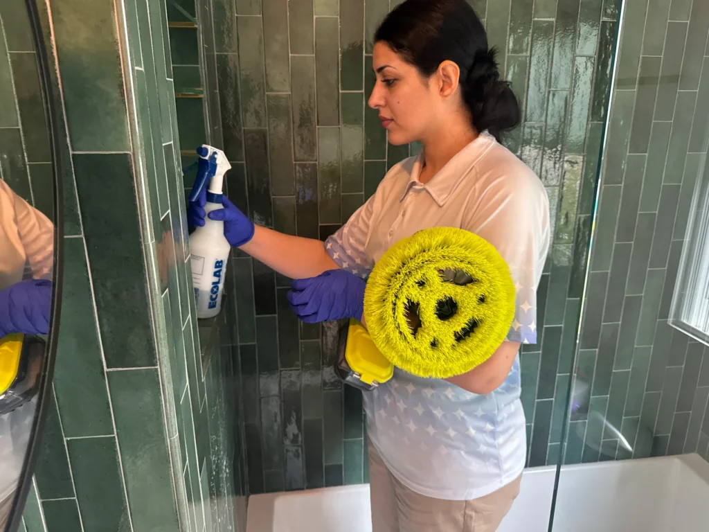 Sygora cleaner with a spray bottle and powered scrub brush in a shower.