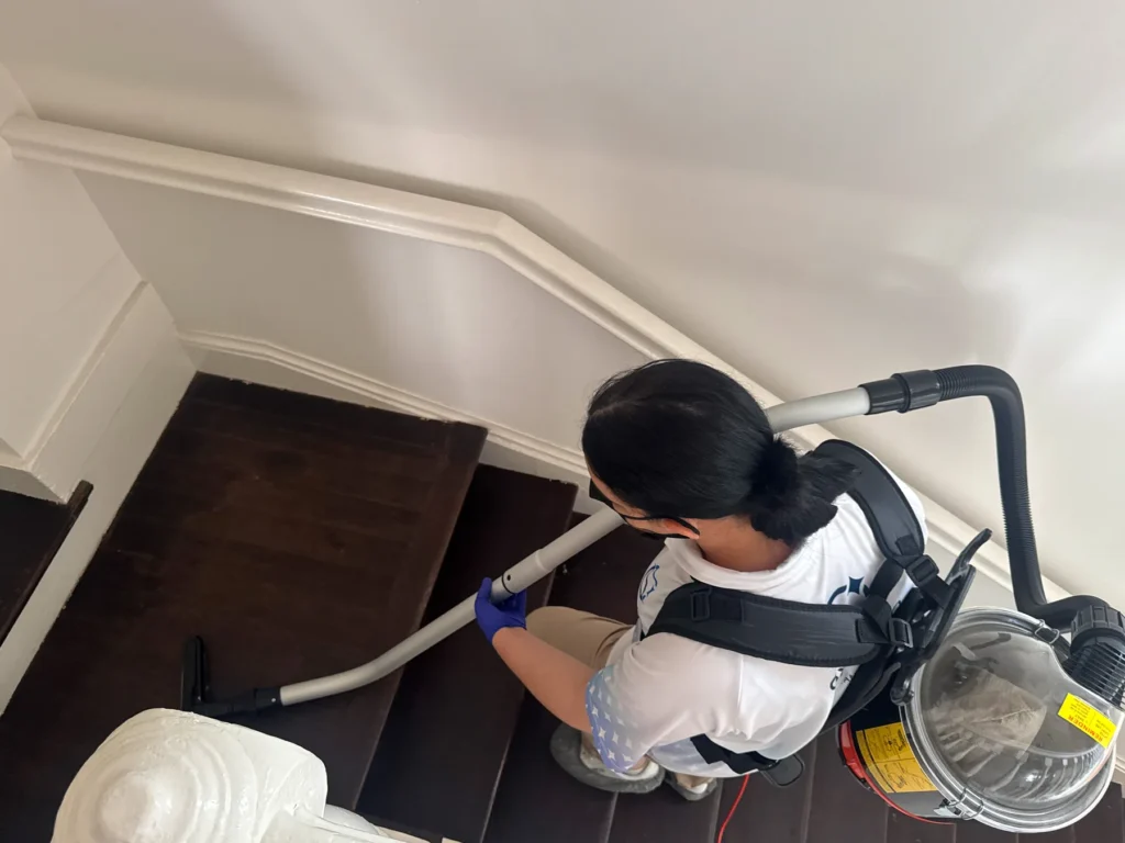 Sygora cleaner vacuuming wooden stairs with a backpack vacuum.